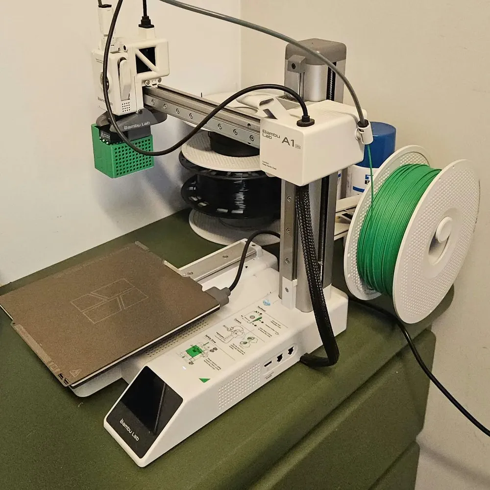 A impressora 3D Bambu Lab A1 mini, em casa, com um carretel de filamento verde